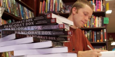 Nathan J.S. Marchand author with pile of copies of his book Pandora's Box