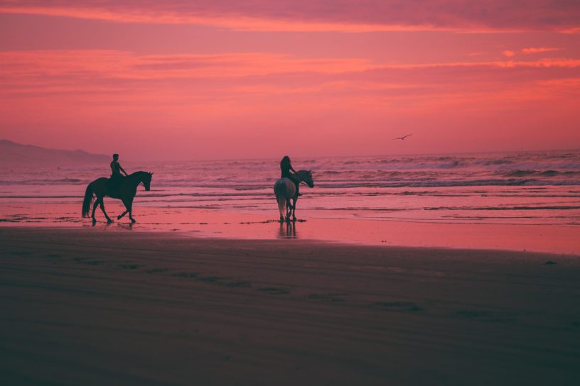 vibrance photo of man and woman on horses by beach. Cormac McCarthy Blood meridian. Photo by Austin Neill on Unsplash