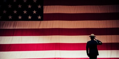 soldier saluting an American flag, illustration for Lawrence Hall speech for Armistice Day/Remembrance Day/Veterans Day. Photo by Brett Sayles: https://www.pexels.com/photo/man-standing-on-stage-facing-an-american-flag-1340504/