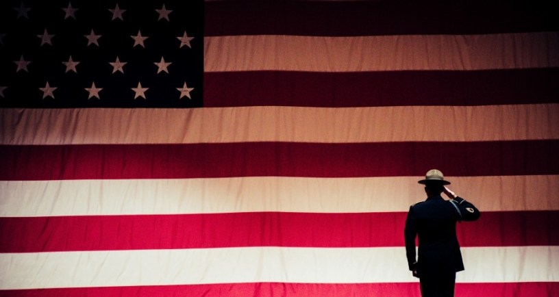 soldier saluting an American flag, illustration for Lawrence Hall speech for Armistice Day/Remembrance Day/Veterans Day. Photo by Brett Sayles: https://www.pexels.com/photo/man-standing-on-stage-facing-an-american-flag-1340504/
